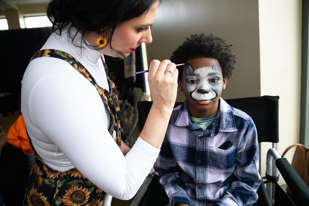 woman painting an animal face on a boy.